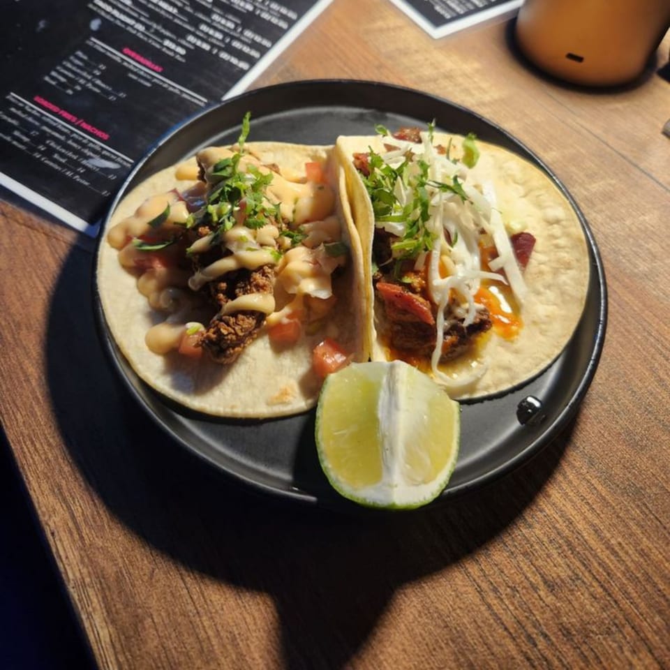 Two delicious tacos with various toppings and a lime wedge on a dark plate at The Taco Bar.