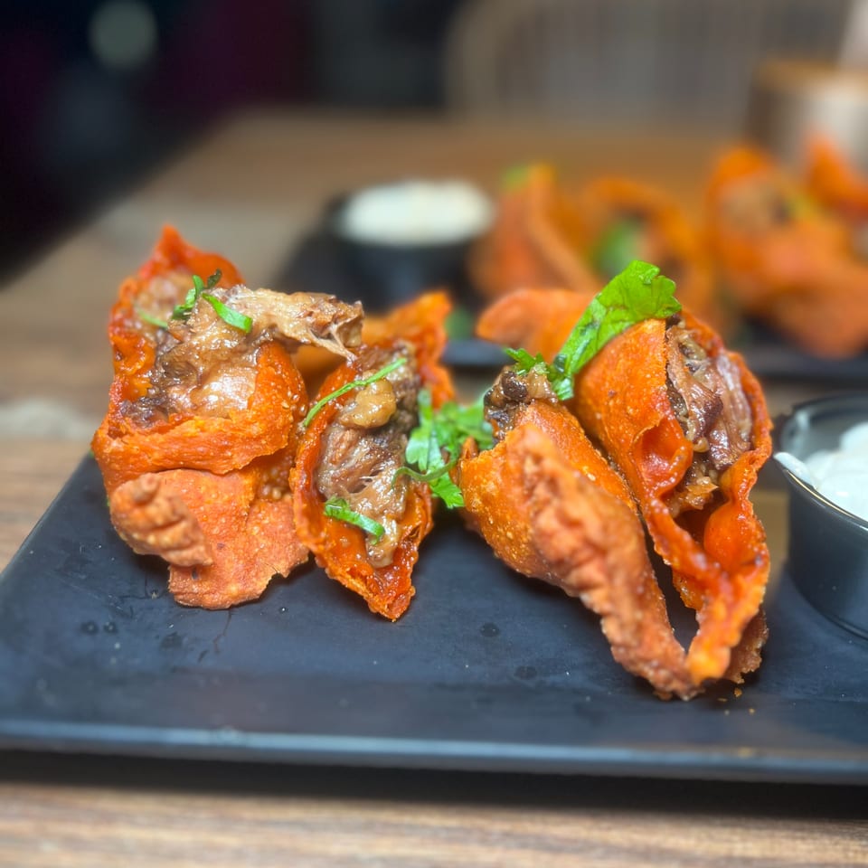 Crispy orange taco shells filled with shredded meat and green herbs, served on a black plate.