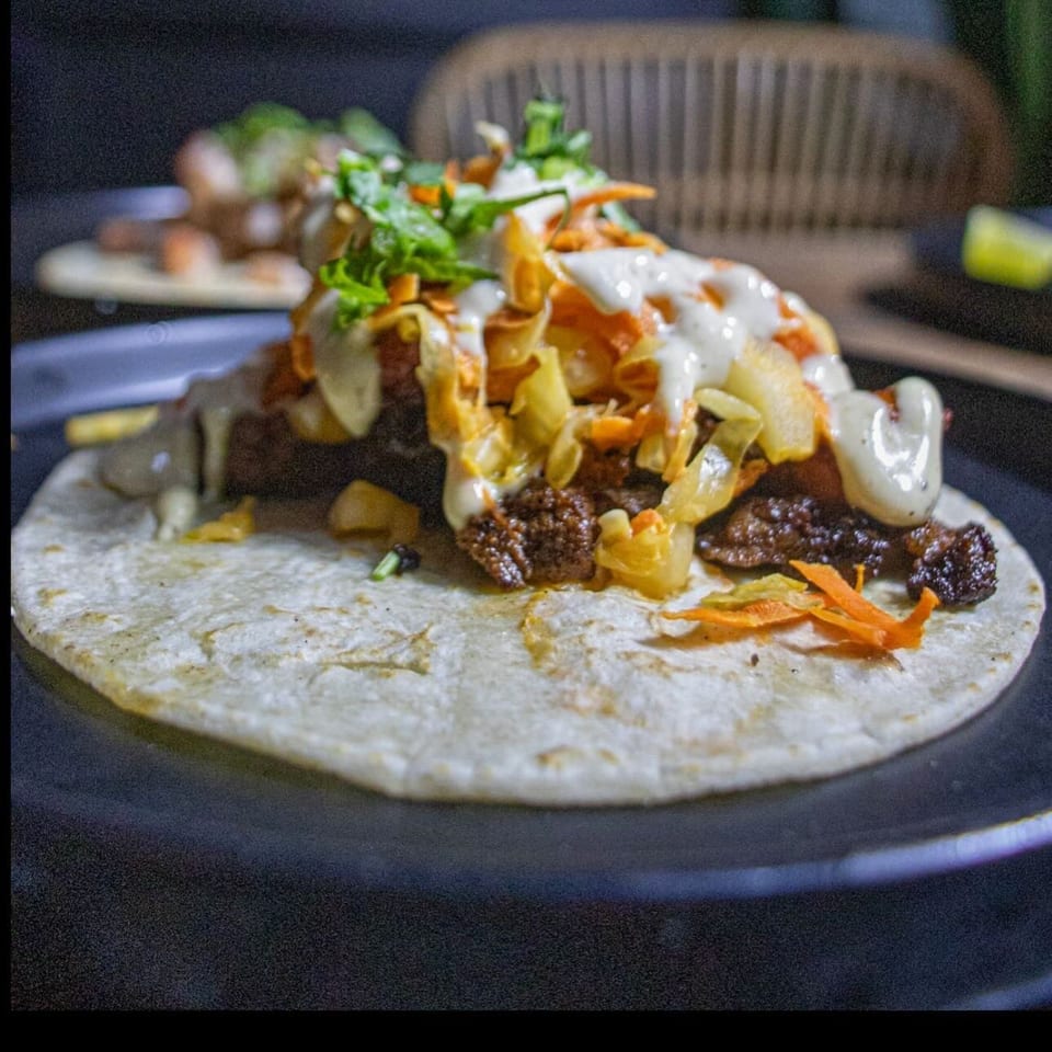 A delicious Mexican taco from The Taco Bar, topped with meat, vegetables, and a creamy sauce.