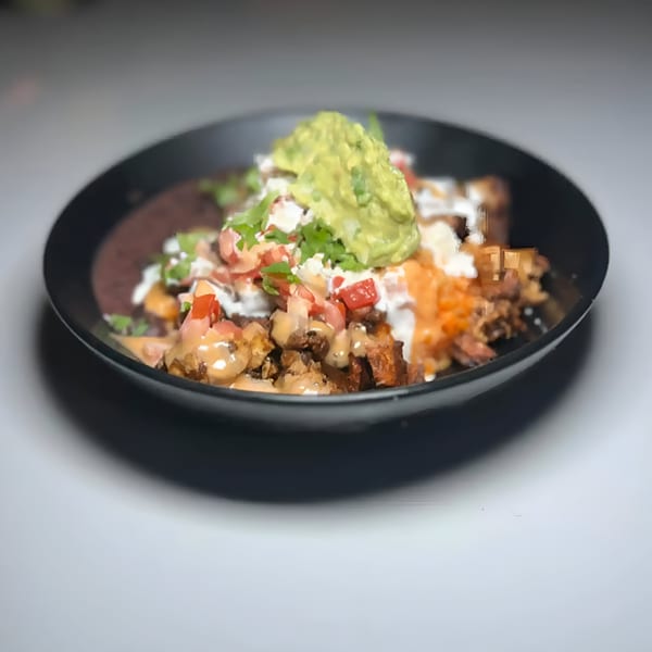 A black bowl of The Taco Bar's Mexican food, topped with guacamole, pico de gallo, and sauces.