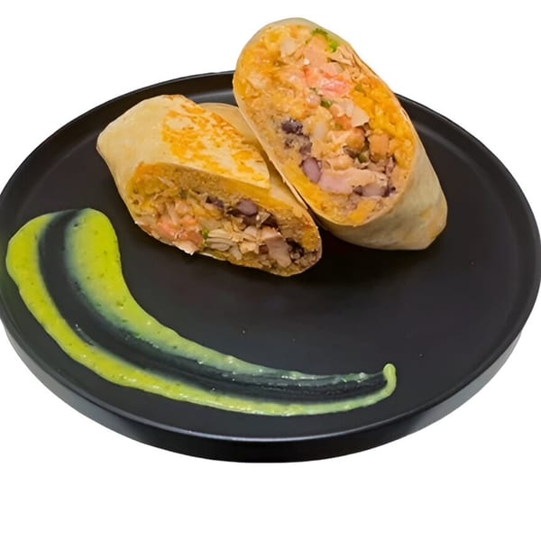Two halves of a burrito filled with meat, beans, and rice, with green sauce on a black plate.