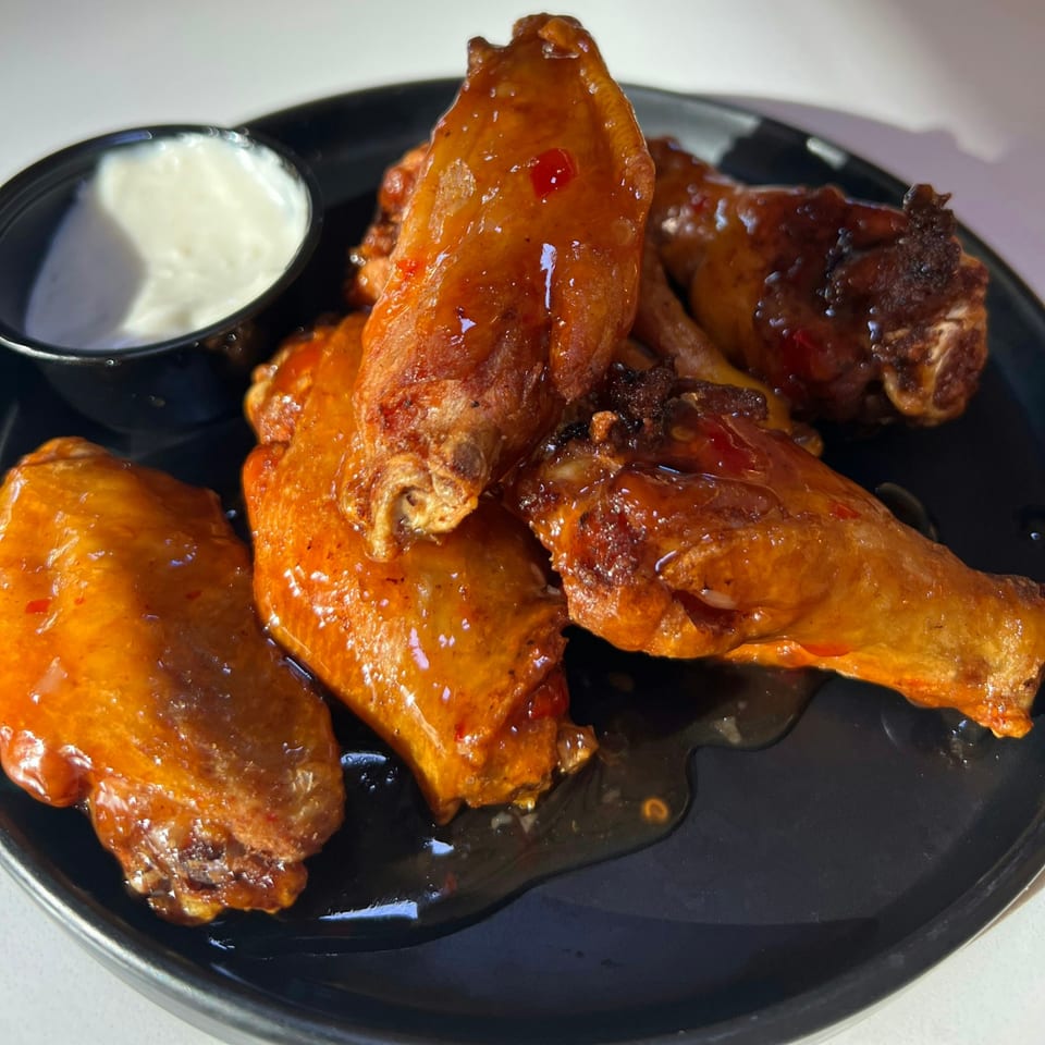 A black plate holds several glossy, orange-glazed chicken wings with a side of white dipping sauce.